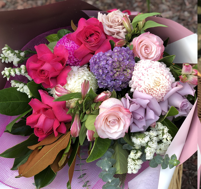 A bouquet of various flowers including pink roses, white hydrangeas, and purple blooms wrapped in pink and white paper.