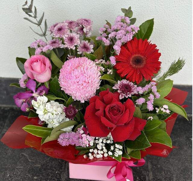 A colorful arrangement of various flowers including roses, chrysanthemums, and baby's breath, displayed in a pink container.