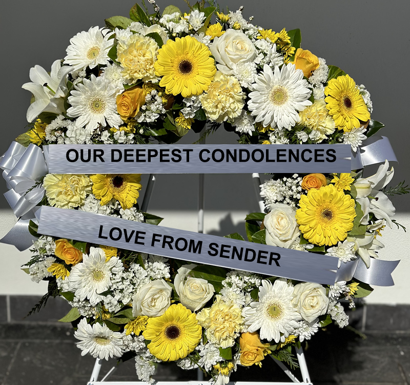 A flower wreath with yellow and white blossoms and two ribbons. The top ribbon reads, "OUR DEEPEST CONDOLENCES," and the bottom ribbon reads, "LOVE FROM SENDER.