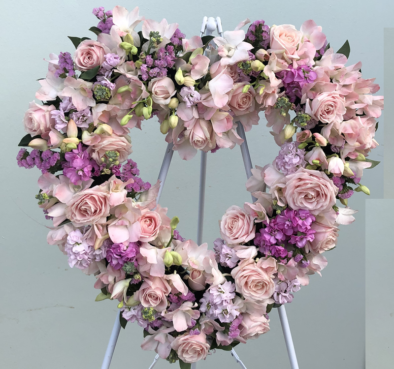 A heart-shaped floral arrangement with pink and purple flowers displayed on an easel.